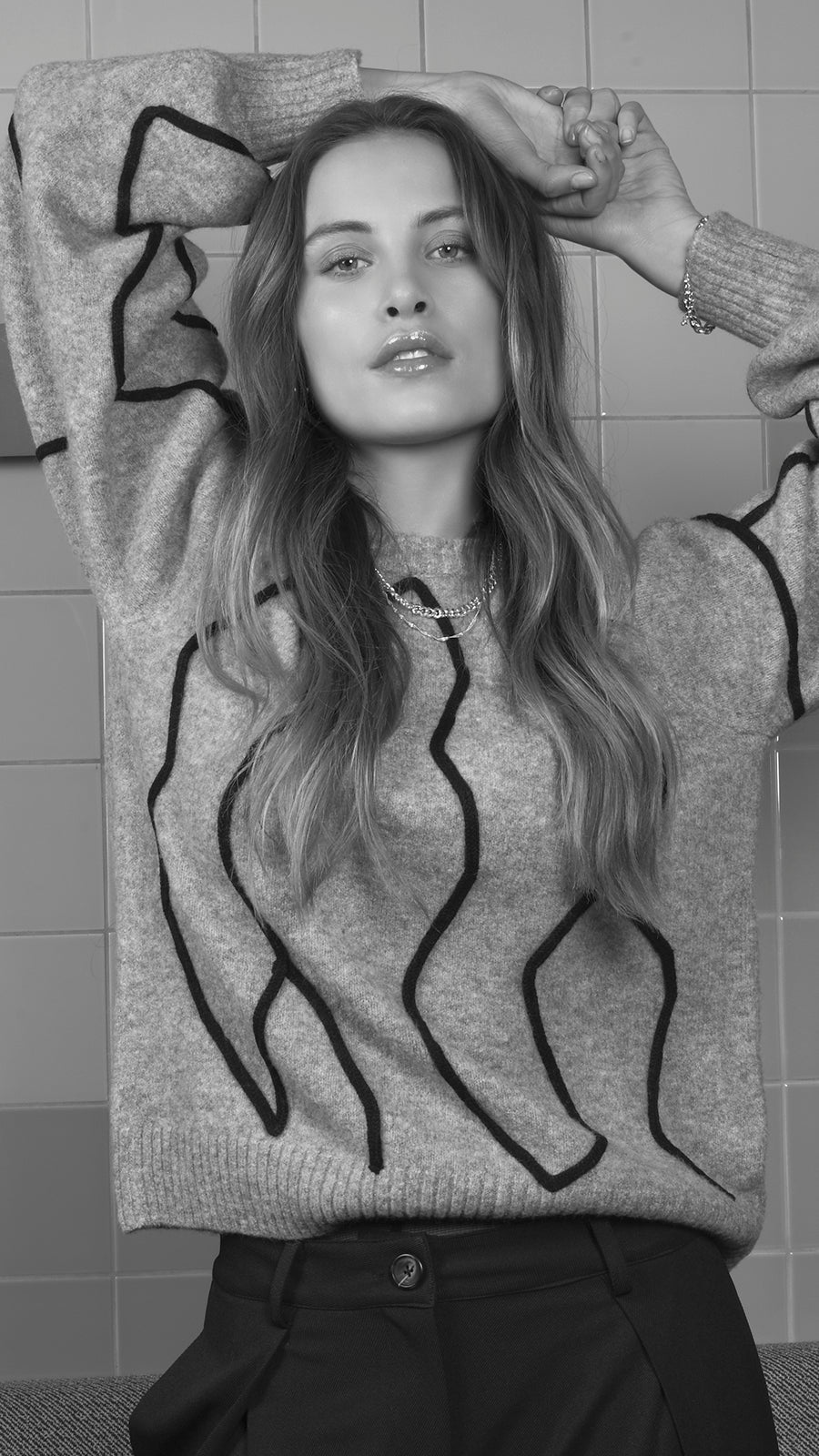 Een vrouw draagt een grijze trui met zwart patroon.