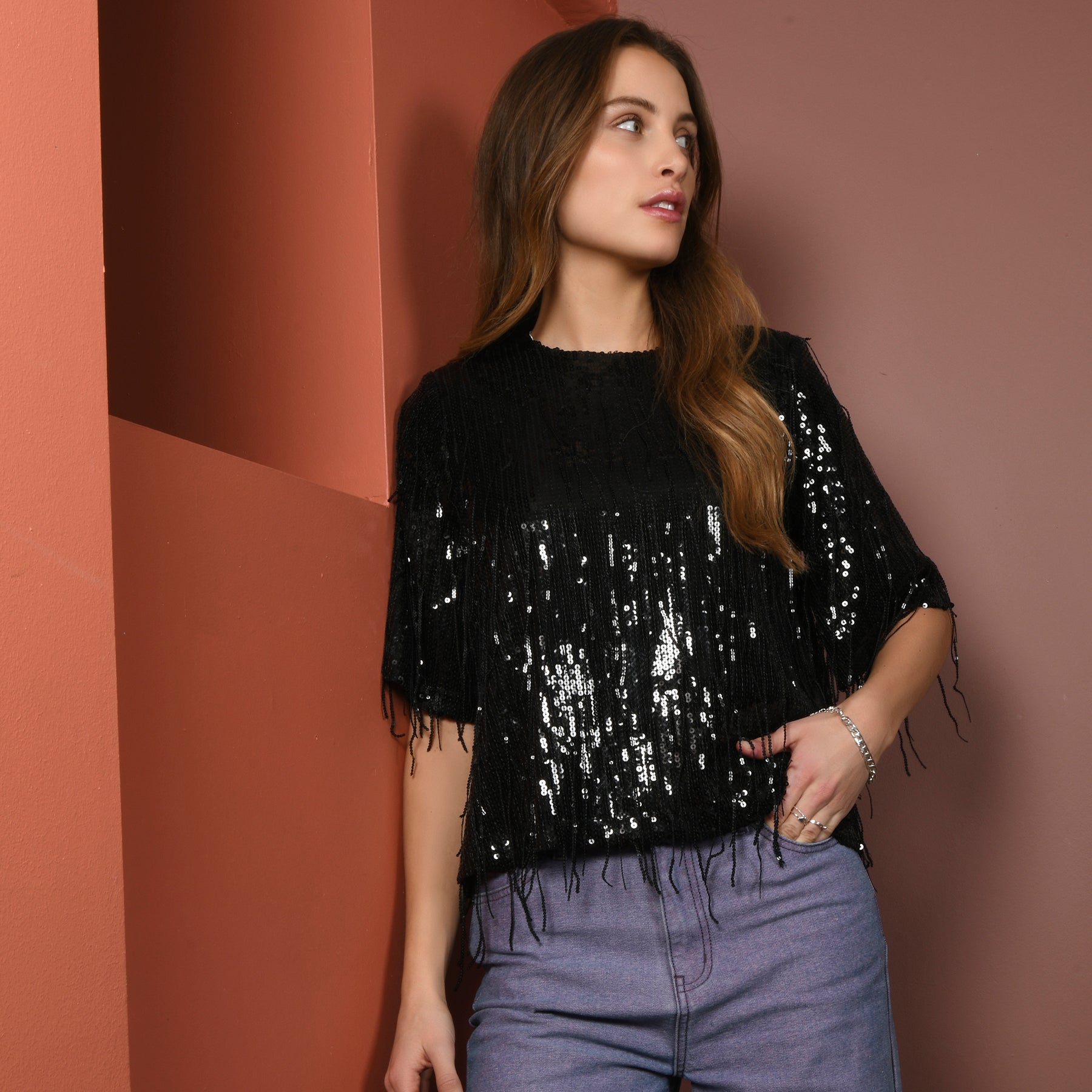 Een vrouw in een glanzende zwarte top met jeans.